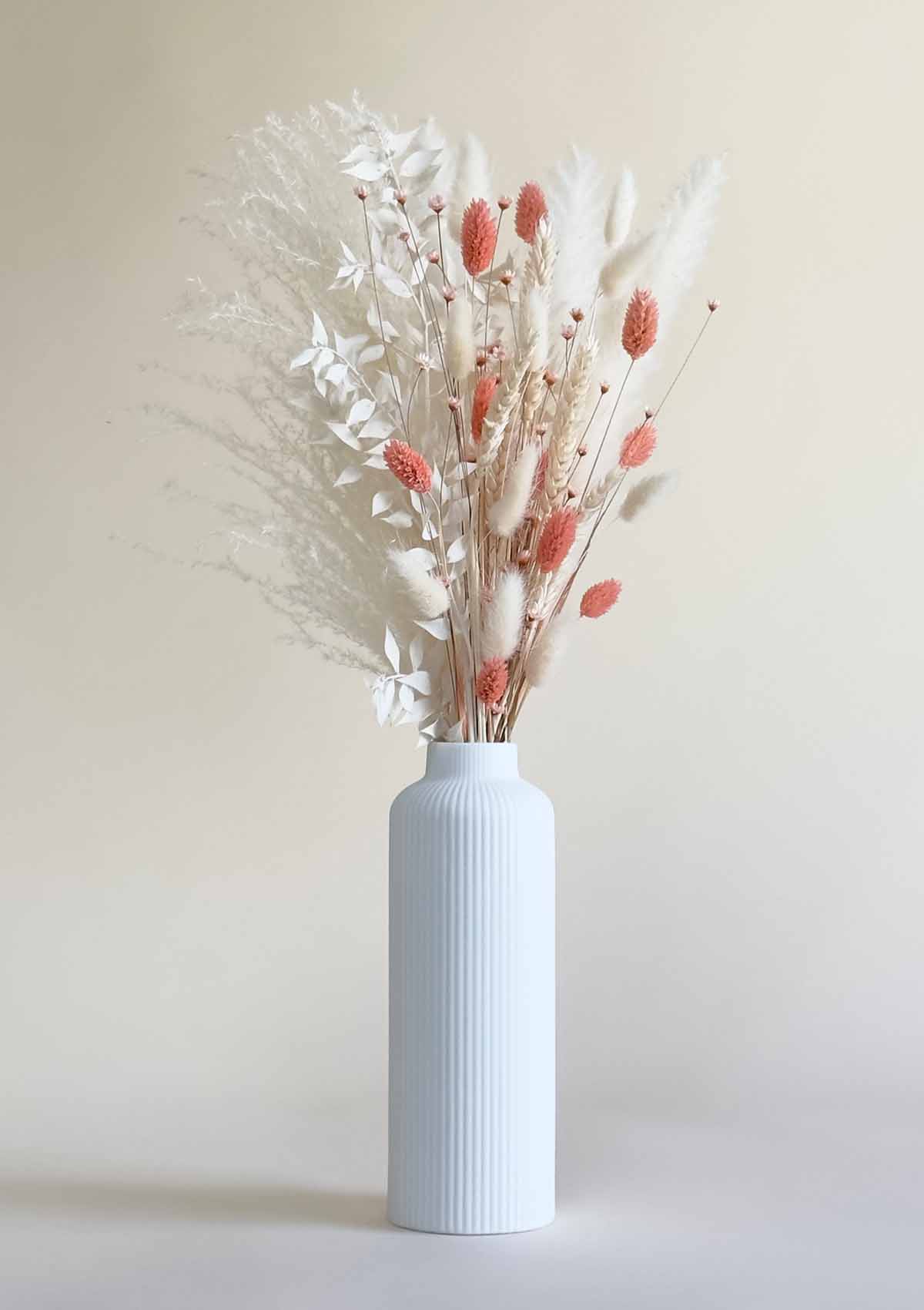 Trockenblumenstrauss in den Farben creme-weiss, rosa und apricot in weißer, schmaler Keramilkvase.